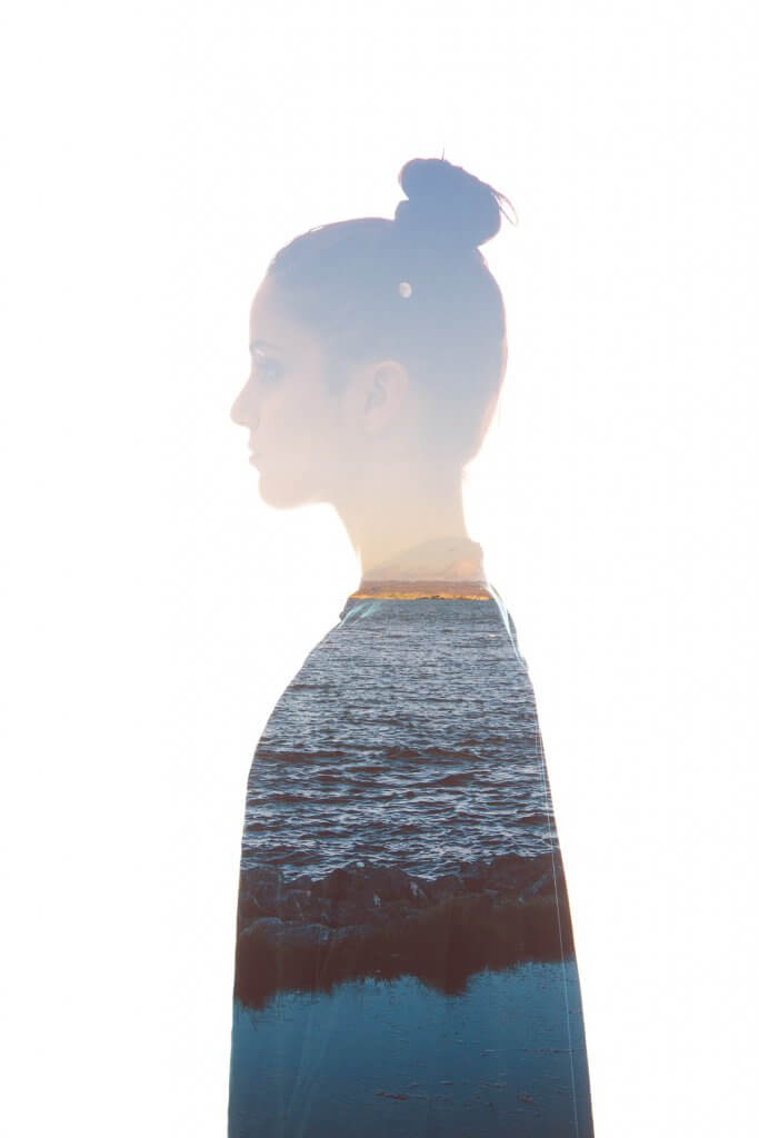 An image of sky, sea and land seen through the outline of a woman standing in profile, at peace.