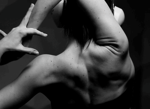 A black and white photo of a woman stretching one arm over her head, elbows bent, big headphones on.