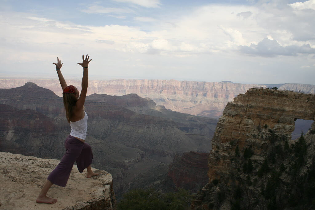 Woman doing a warrior 1 yoga pose on the edge of a rock ravine, very high up.