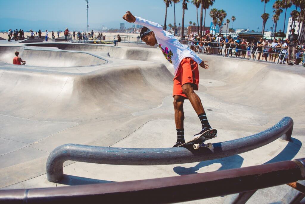 A young man balancing his skateboard precariously on a rail in a skatepark.