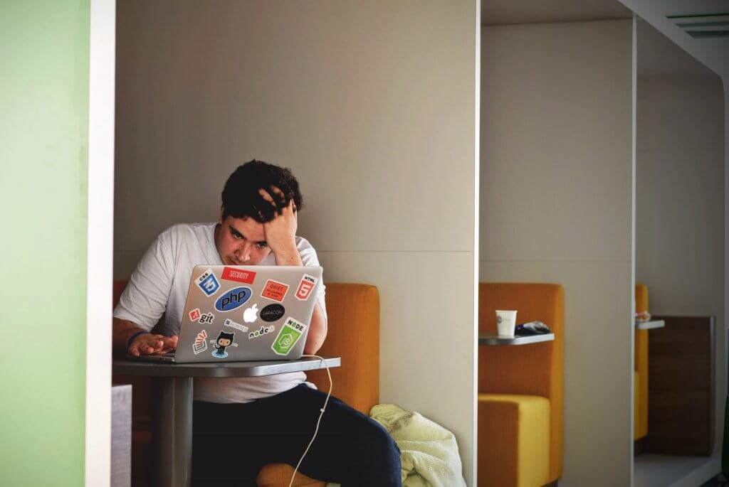 A man sitting at his laptop, running his hands through his hair, clearly stressing out.