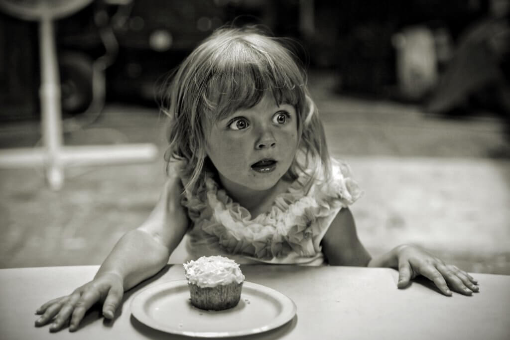 Little girl looking wide-eyed off to the side in surprise at the cake that has just been presented to her.