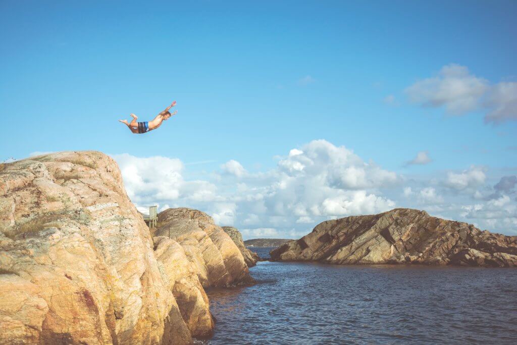 A man mid-dive off a cliff into the sea.