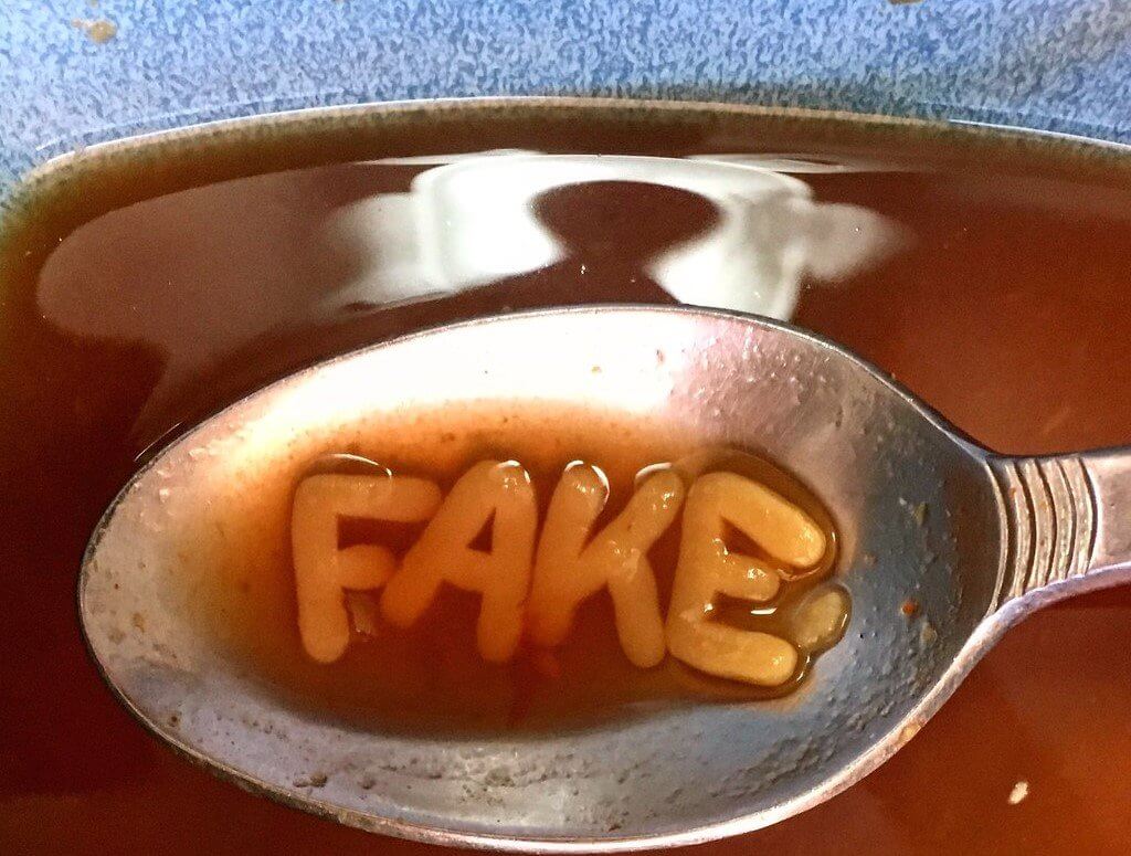 Alphabetti spaghetti letters spell out 'FAKE' on a spoon being used to eat red soup.