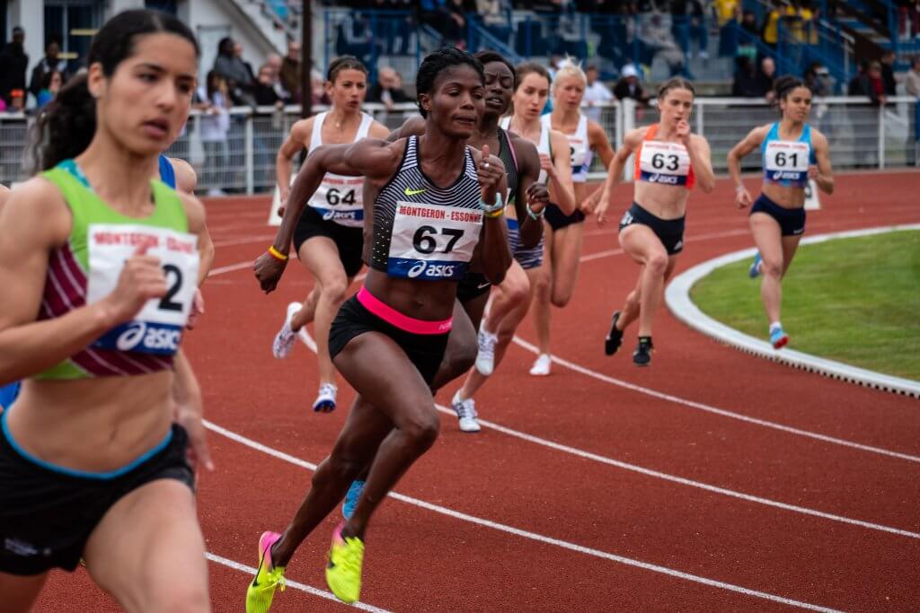 Female athletes racing on a track in a stadium.