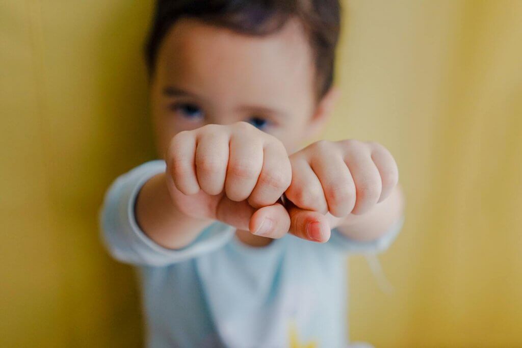 A toddler with both fists up in front of his face.