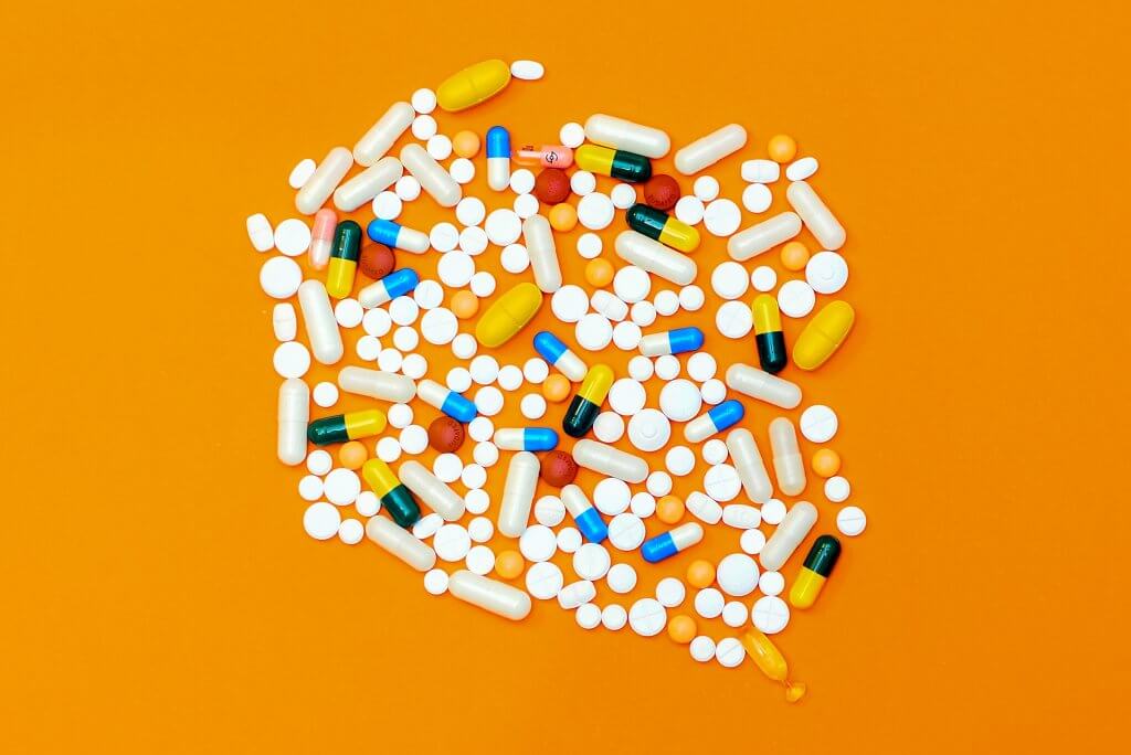 An eclectic mixture of lots of different kinds of pills laid out on a bright orange background.